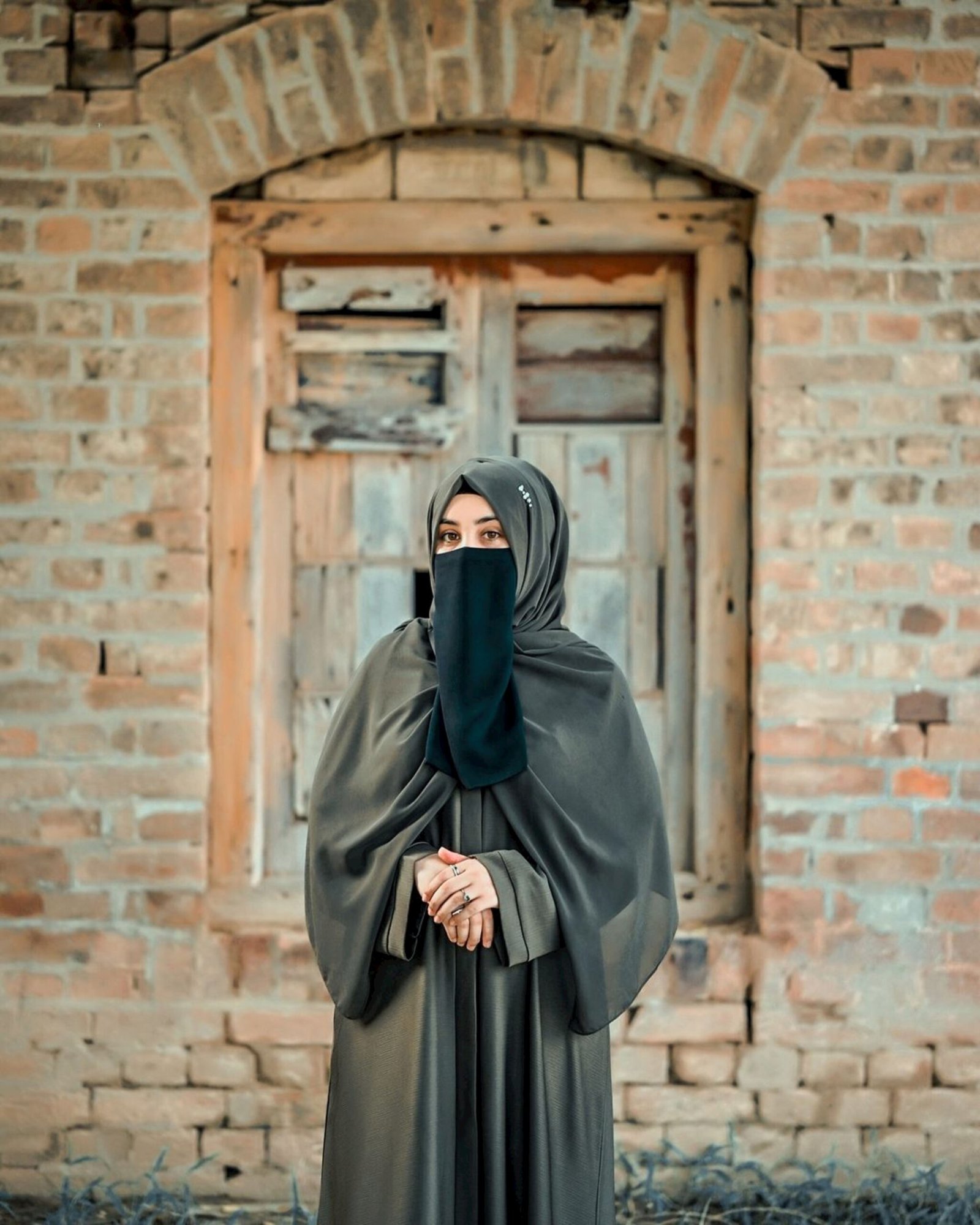 A woman wearing a black veil standing in front of a brick building